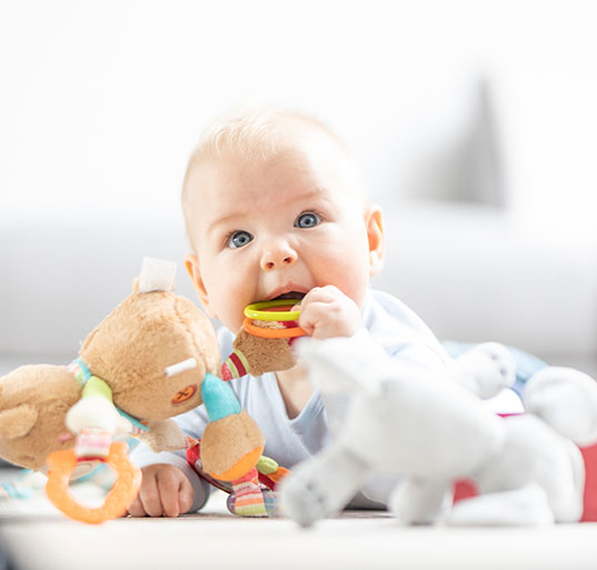 Curious baby chewing on a colorful teether toy while engaging in sensory play to support early brain development skills.